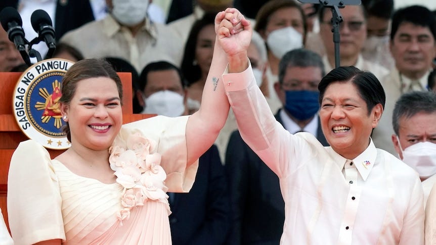 A woman and a man standing on a stage raise each other's hands