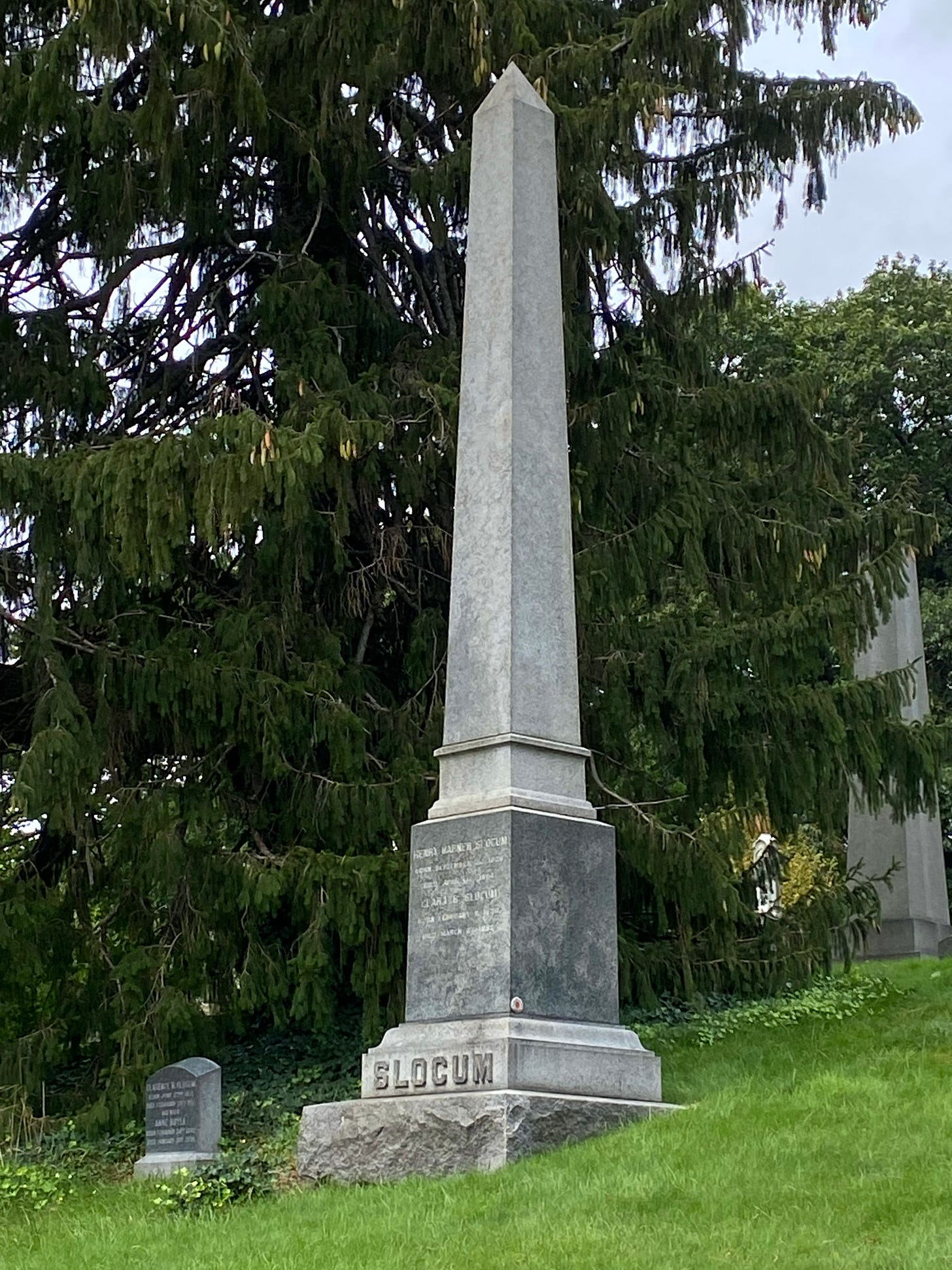 A tall obelisk with SLOCUM engraved at the base in large letters amidst green trees and bright grass.