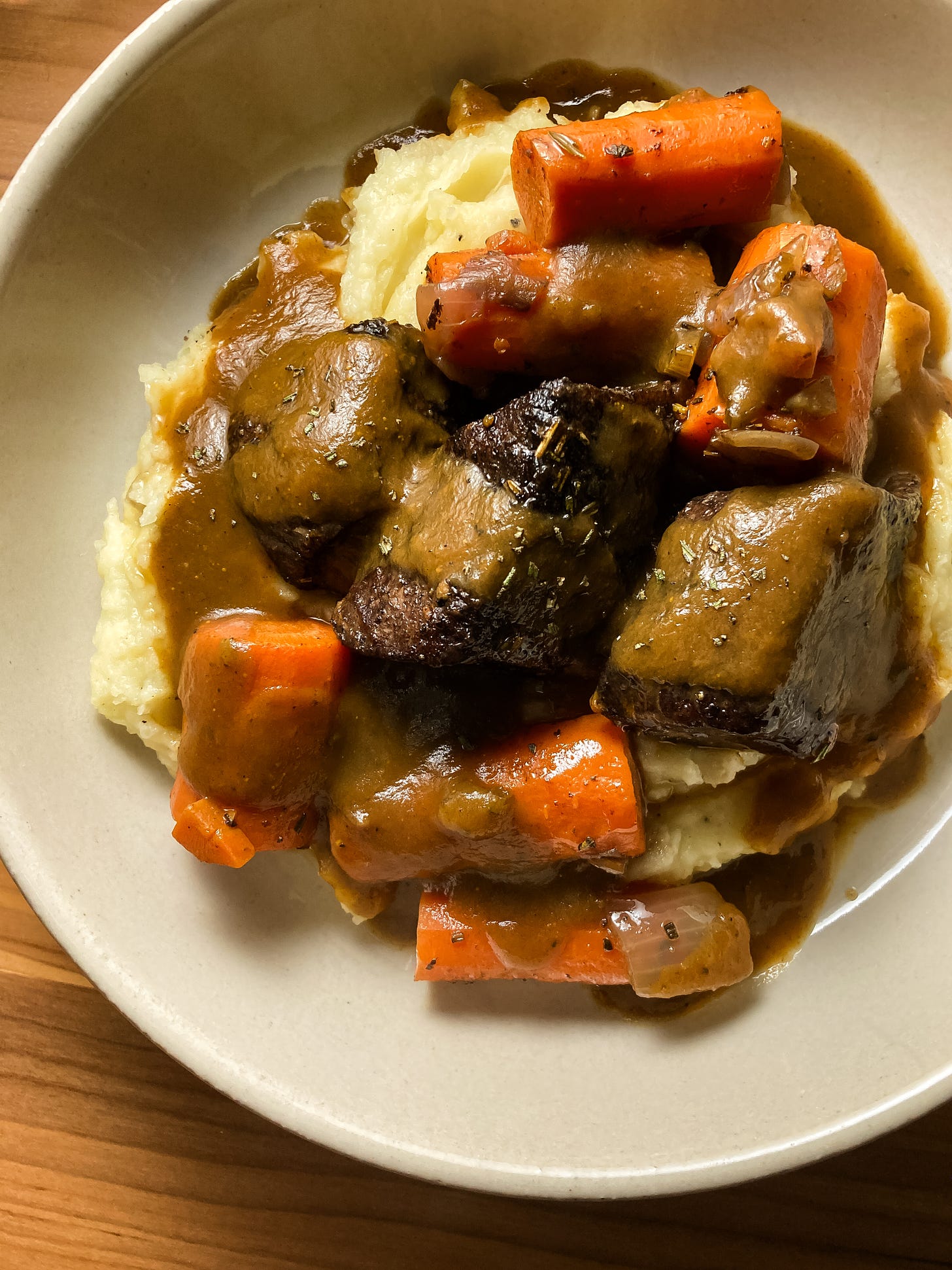 Close-up of braised short ribs and carrots over mashed potatoes, draped in gravy.