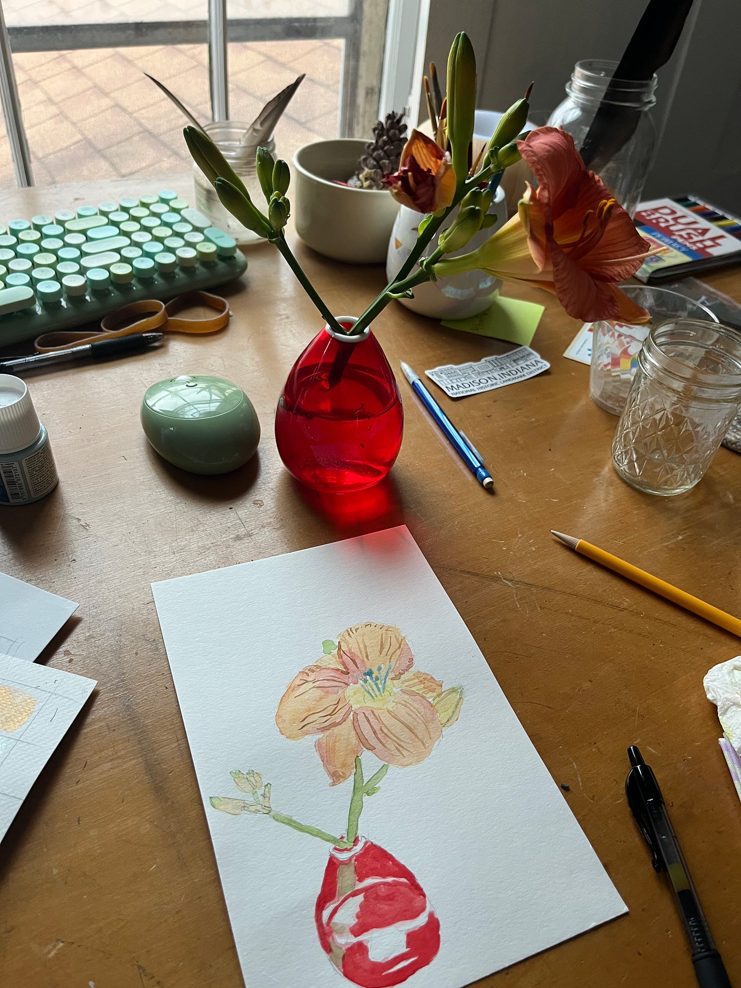 A picture of a desk with a vase of day lilies, one dead and one blooming and sitting in front of it, an unfinished watercolor painting of the vase and the lilies A picture of a desk with a vase of day lilies, one dead and one blooming and sitting in front of it, an unfinished watercolor painting of the vase and the lilies