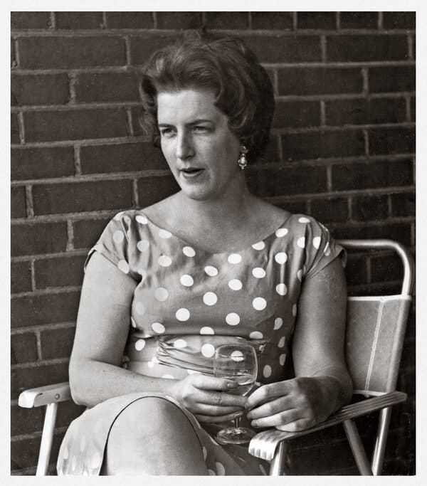 A black and white photo of Yvonne Barr sitting in front of a brick wall and wearing a dress with polka dots.