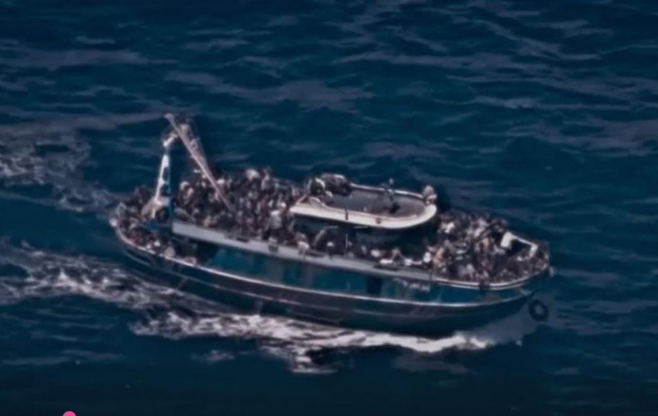 A grainy surveillance picture of an rusty boat overloaded with people