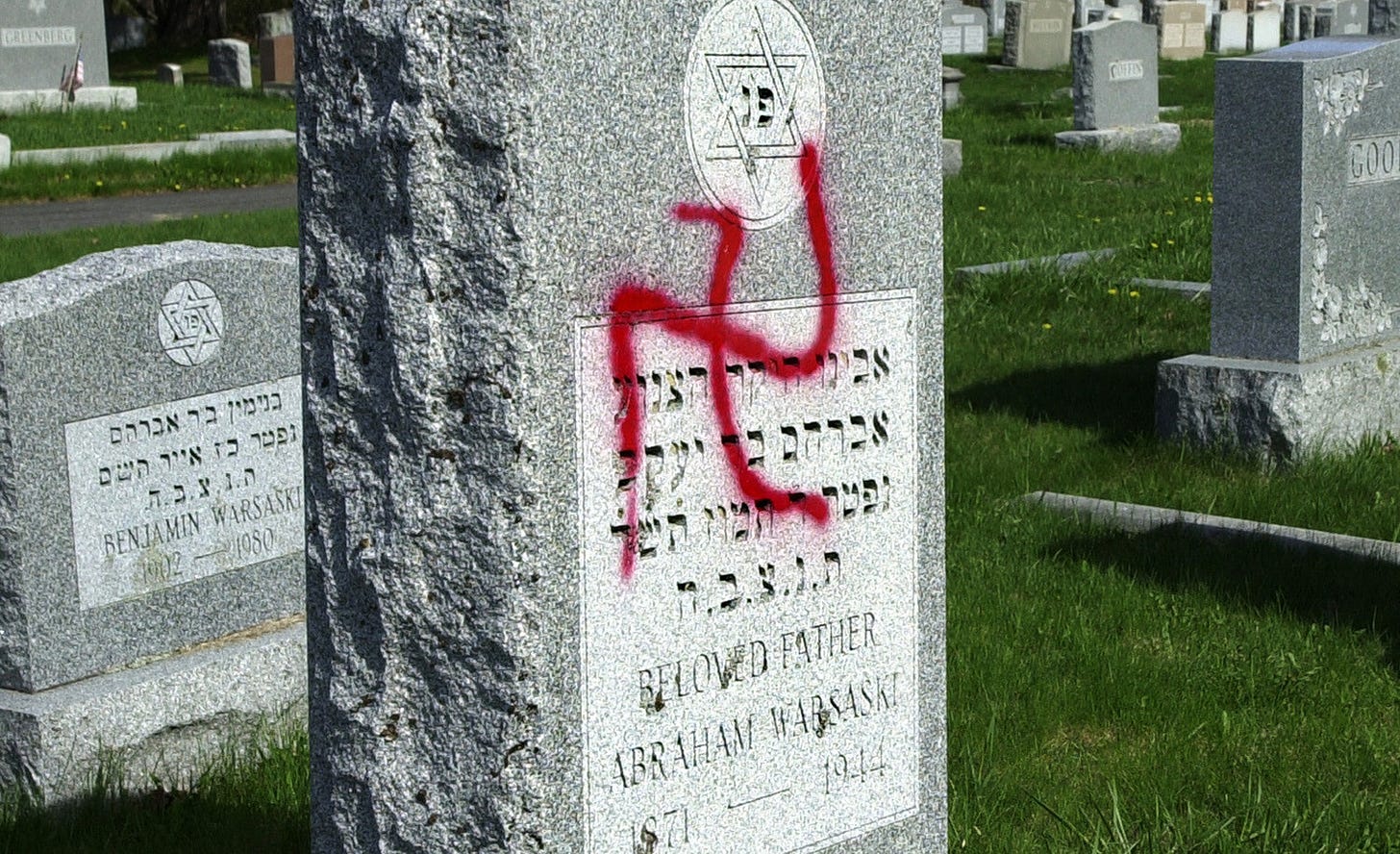 Image of a swastika spray painted onto a gravestone with a Star of David and Hebrew script