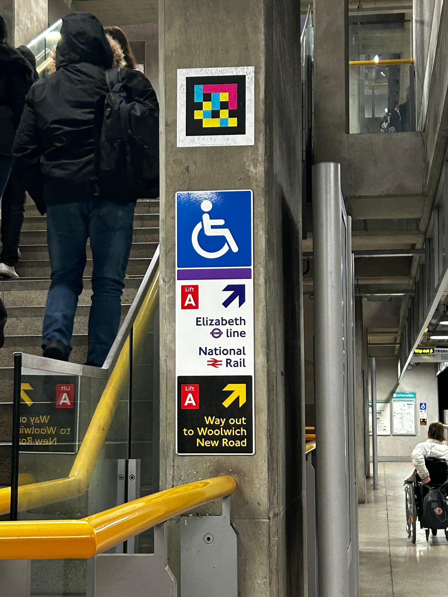 Navilens QR code next to a staircase above a wheelchair sign and a sign to National Rail and the Elizabeth Line