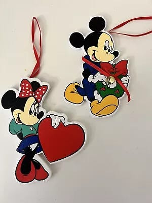 2 Disney ornaments, one Minnie Mouse in a teal skirt and black skirt holding a heart and one of Mickey Mouse holding a wreath.