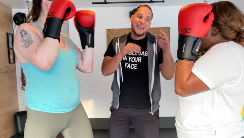Two people face each other, wearing boxing gloves with their arms up next to their heads. 