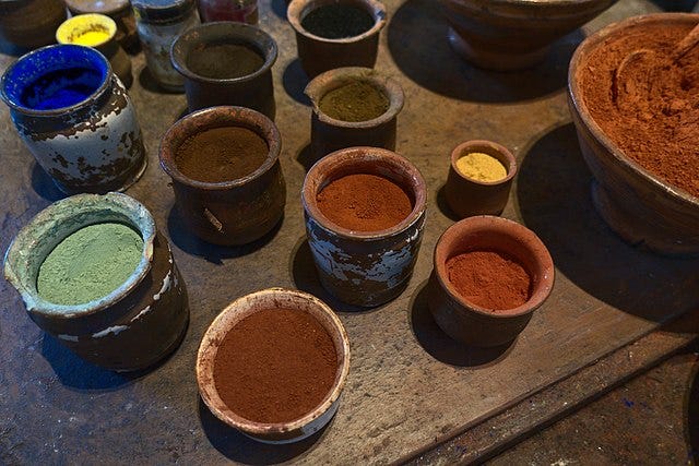 Pots with powders of different colours sit on a wooden table in the Rembrandthuis. These are pigments for paint.