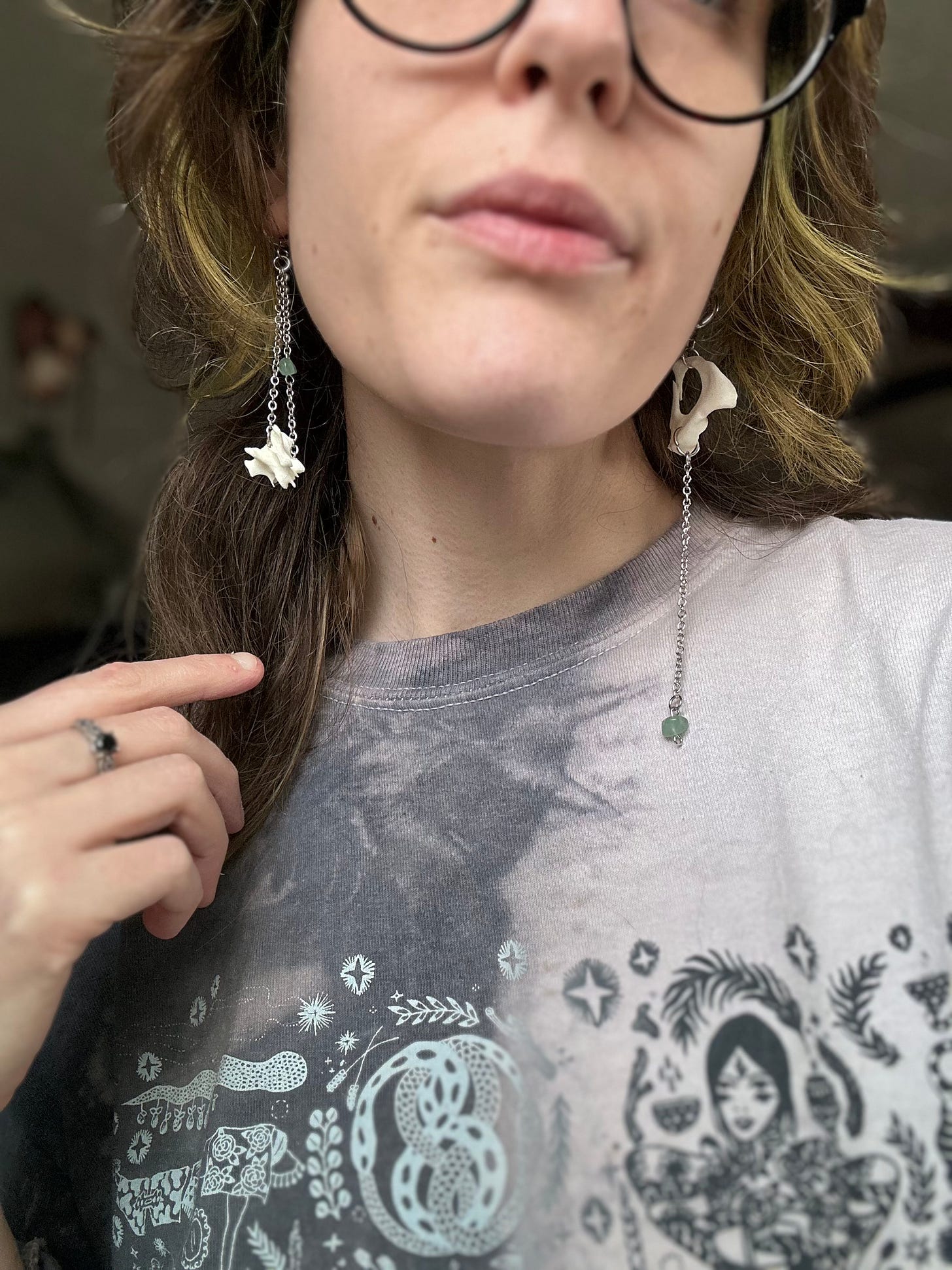 Close up of a person wearing earrings made of bones, thin cable chain, and green aventurine crystals.