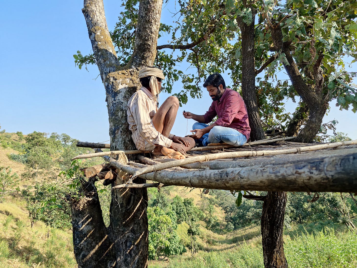 Nitesh talking to a resident of Toranmaal, a hill station in Nandurbar district while sitting on an elevated platform made up on a tree and surrounded by beautiful greenery