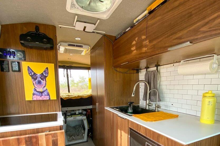 An interior photo of our converted camper van showing dark wood cabinets with white countertops and a large portrait of our Australian cattle dog on a yellow background