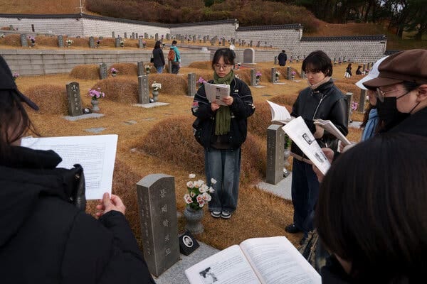 Several people stand in a cemetery, each holding up a text they are looking at.