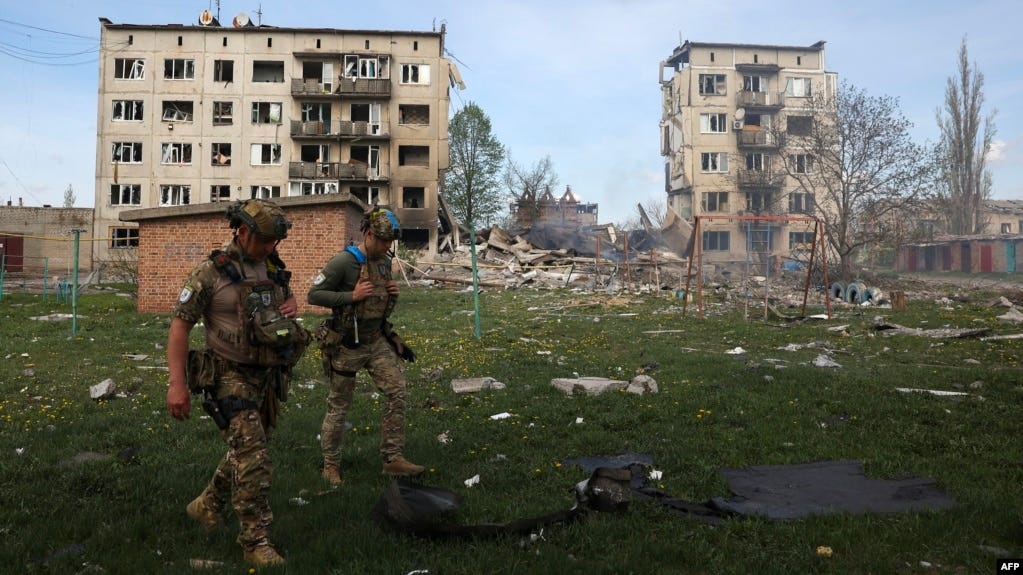 Officers of a special police force walk in front of apartment buildings destroyed by air bombs during the evacuation of local residents from the village of Ocheretine in the Donetsk region on April 15, 2024, amid the Russian invasion in Ukraine.