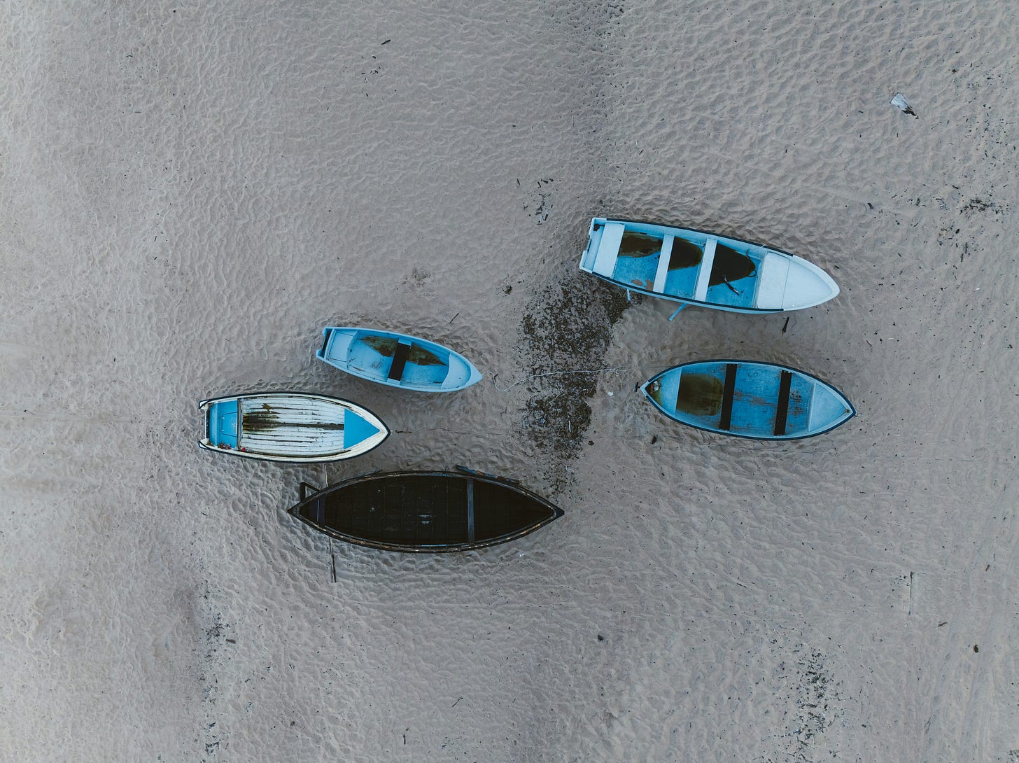 Five blue rowboats sitting on a white sand beach at low tide. 