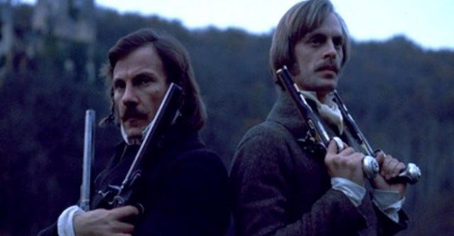 Still from the movie The Duellists. Harvey Keitel and Anthony Carradine are standing back to back, each holding two pistols. 