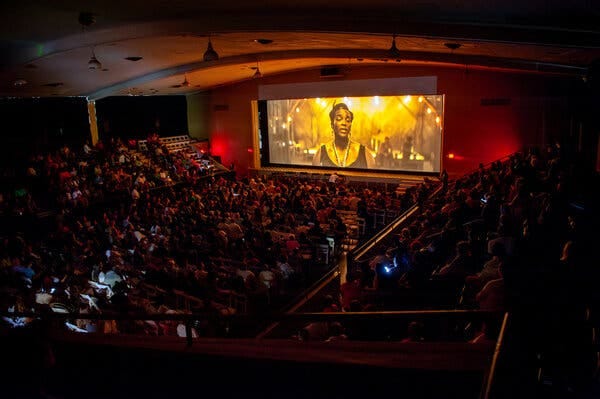 An auditorium is full of people watching a movie on a screen. An auditorium is full of people watching a movie on a screen.