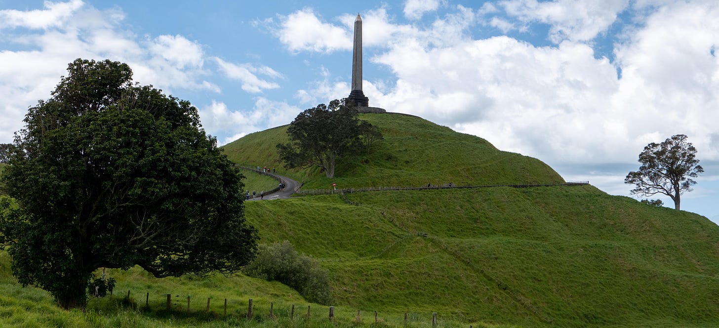 One Tree Hill, with a tall obelisk on top. The grove of trees is on the far side, so not visible. The rings of terracing are clearly visible.