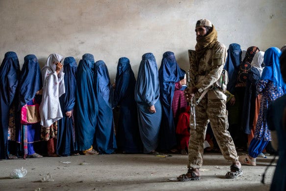 A Taliban fighter stands guard as women wait to receive food rations, in Kabul, Afghanistan, last year.