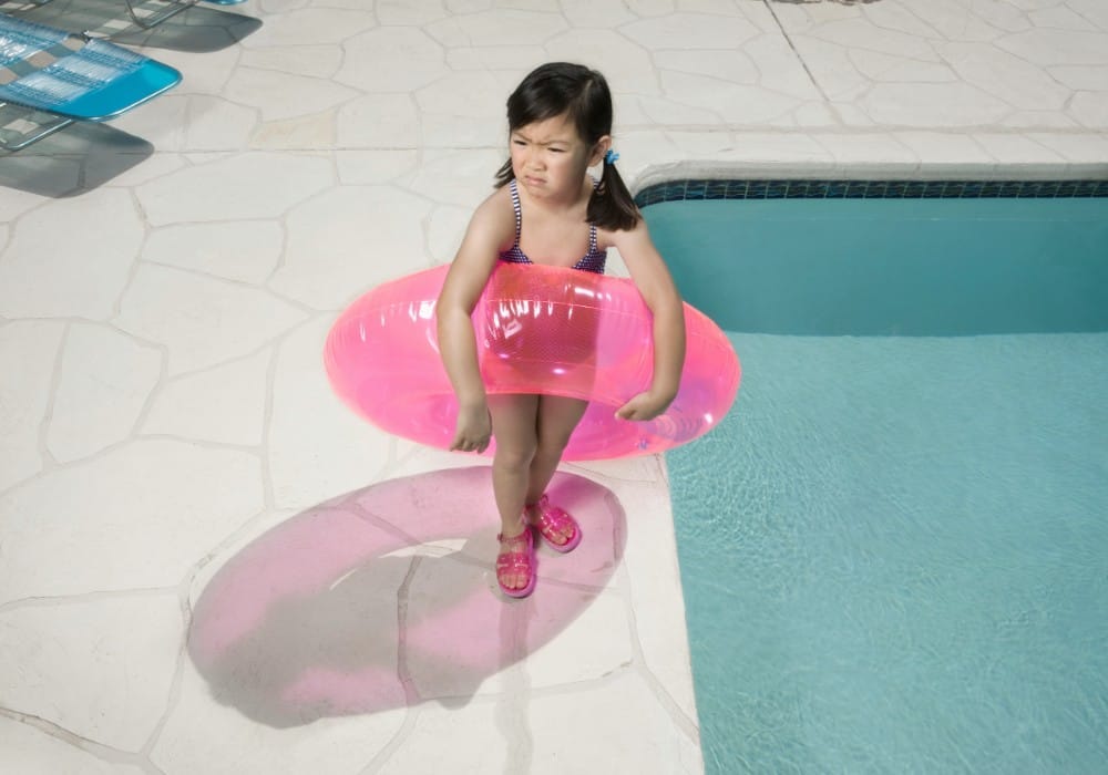 Asian child with hot pink innertube standing by pool with humorous frown on her face