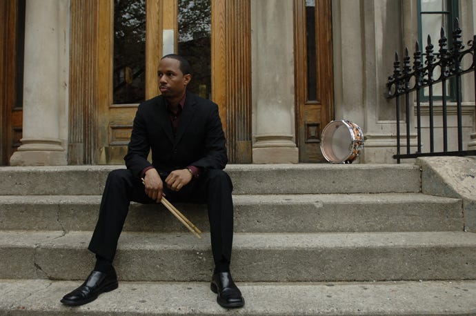 Willie Jones III sitting on stairs holding drumsticks