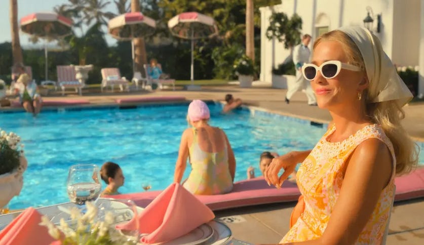 A screenshot from Palm Royale showing a blonde woman lounging at an outdoor table by a pool