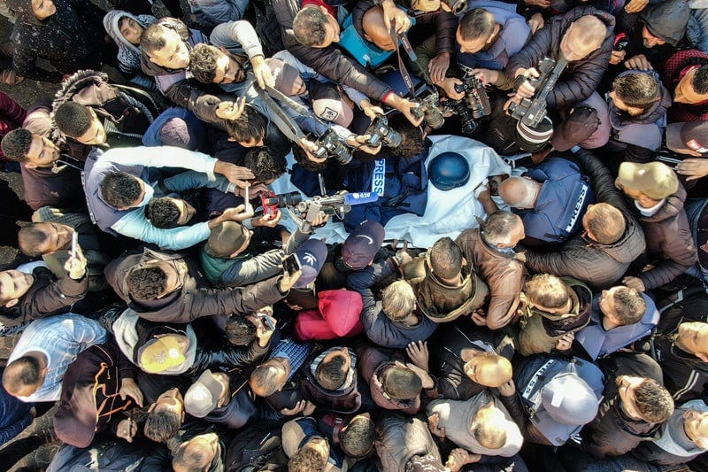 A crowd seen from above surrounds a stretcher with a press helmet A crowd seen from above surrounds a stretcher with a press helmet