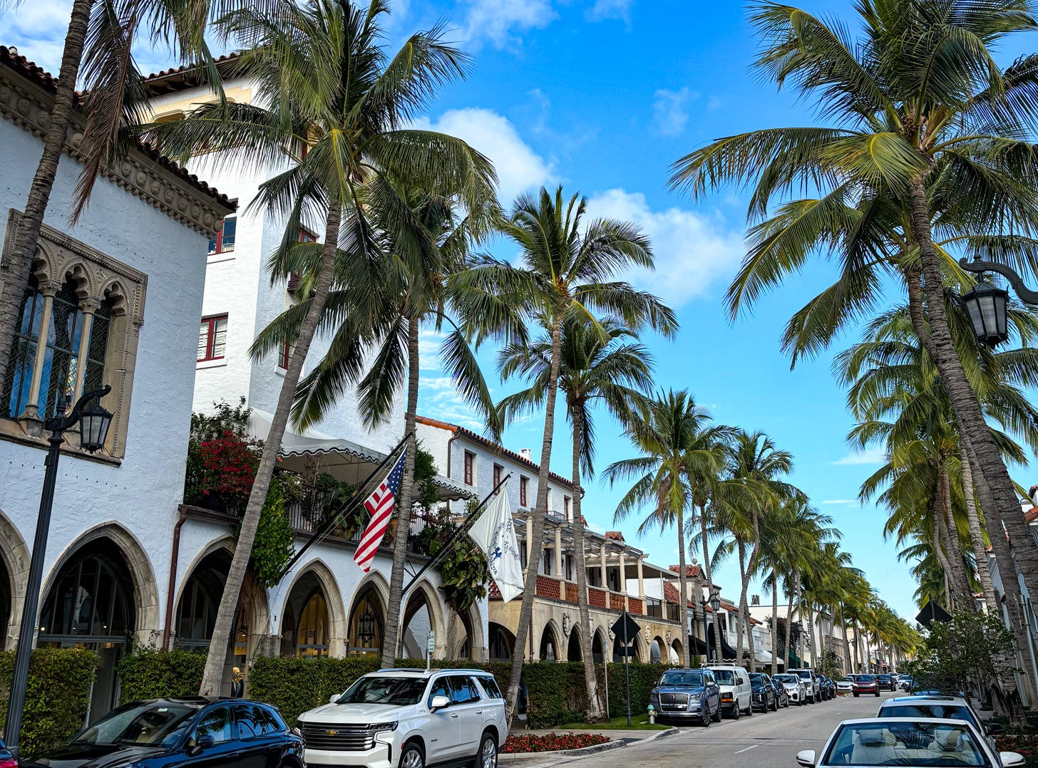 Worth Avenue storefronts with cars parked along the street and tall palm trees on either side