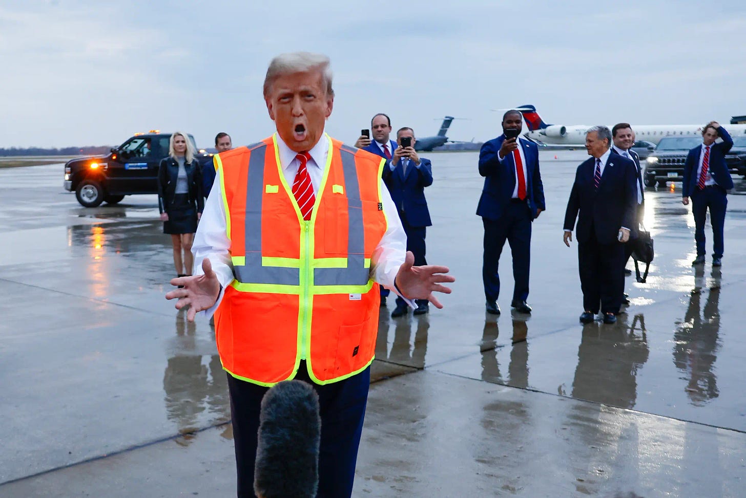 trump orange in the face, stands in orange face in front of a large microphone