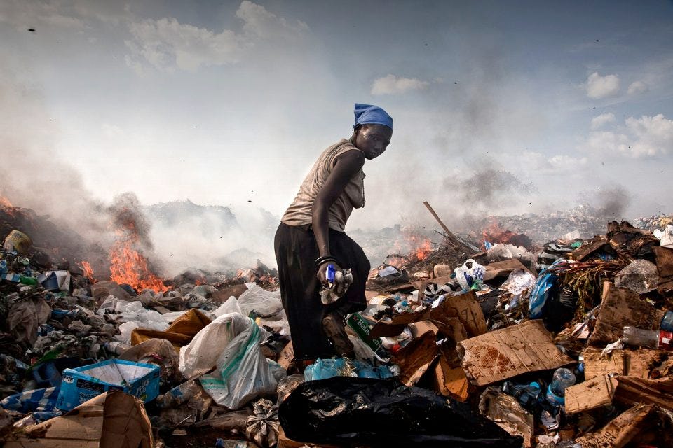 A young black woman in Sudan picking trash in a smoldering burning dump.