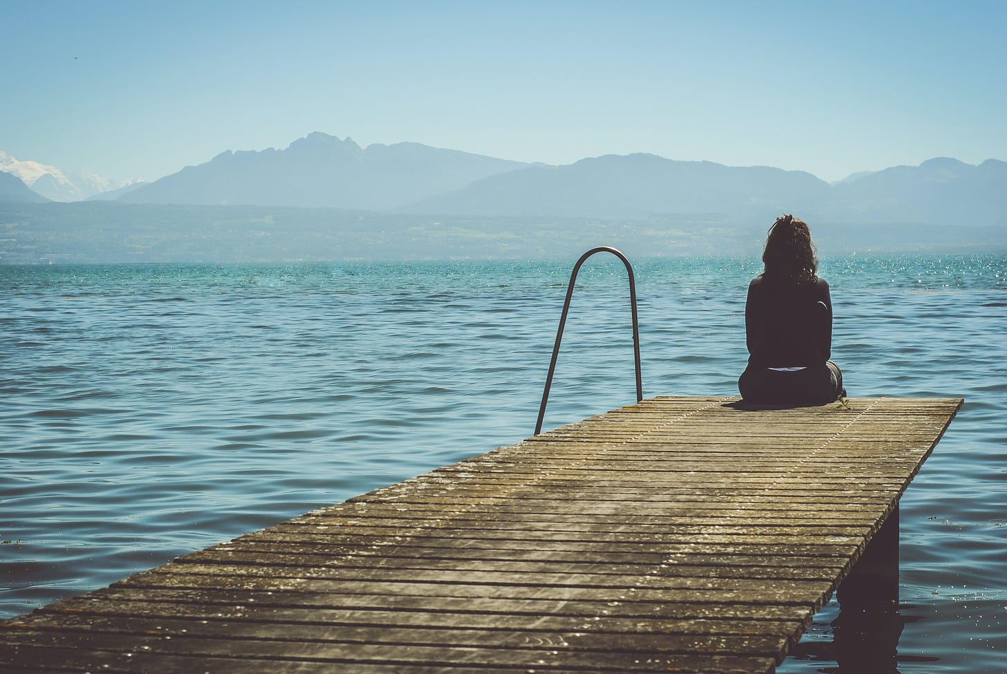 Woman sitting on dock looking at lake and mountains