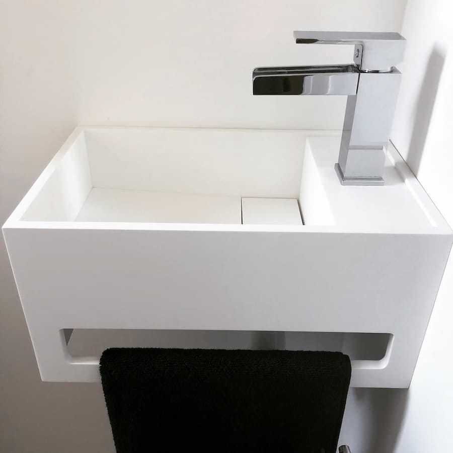 Modern white bathroom sink with a chrome tap. A black towel is hanging on a towel rail, which is integrated into the sink design.