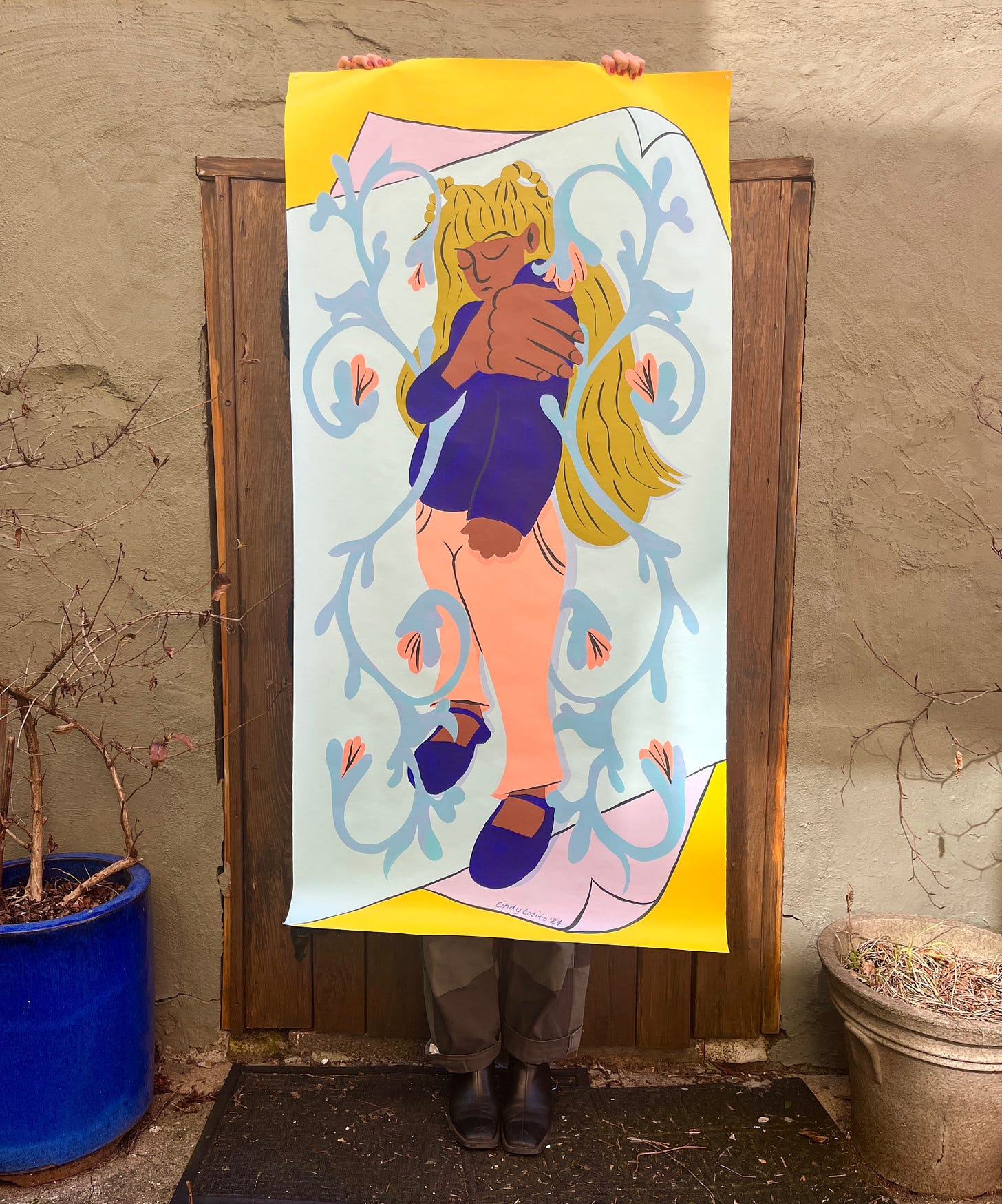 Me holding a life-size mural cloth of a character holding her shoulder amid swirling floral motifs