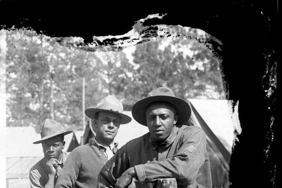 Three African American soldiers pose against a fence at Camp Logan.