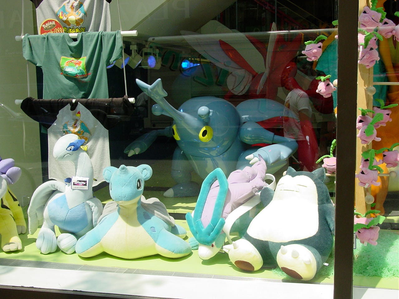 Another photograph of the window display taken from outside the store, showing a Heracross statue and various large plushies, including Lugia, Lapras, Suicune, Raikou, and Snorlax