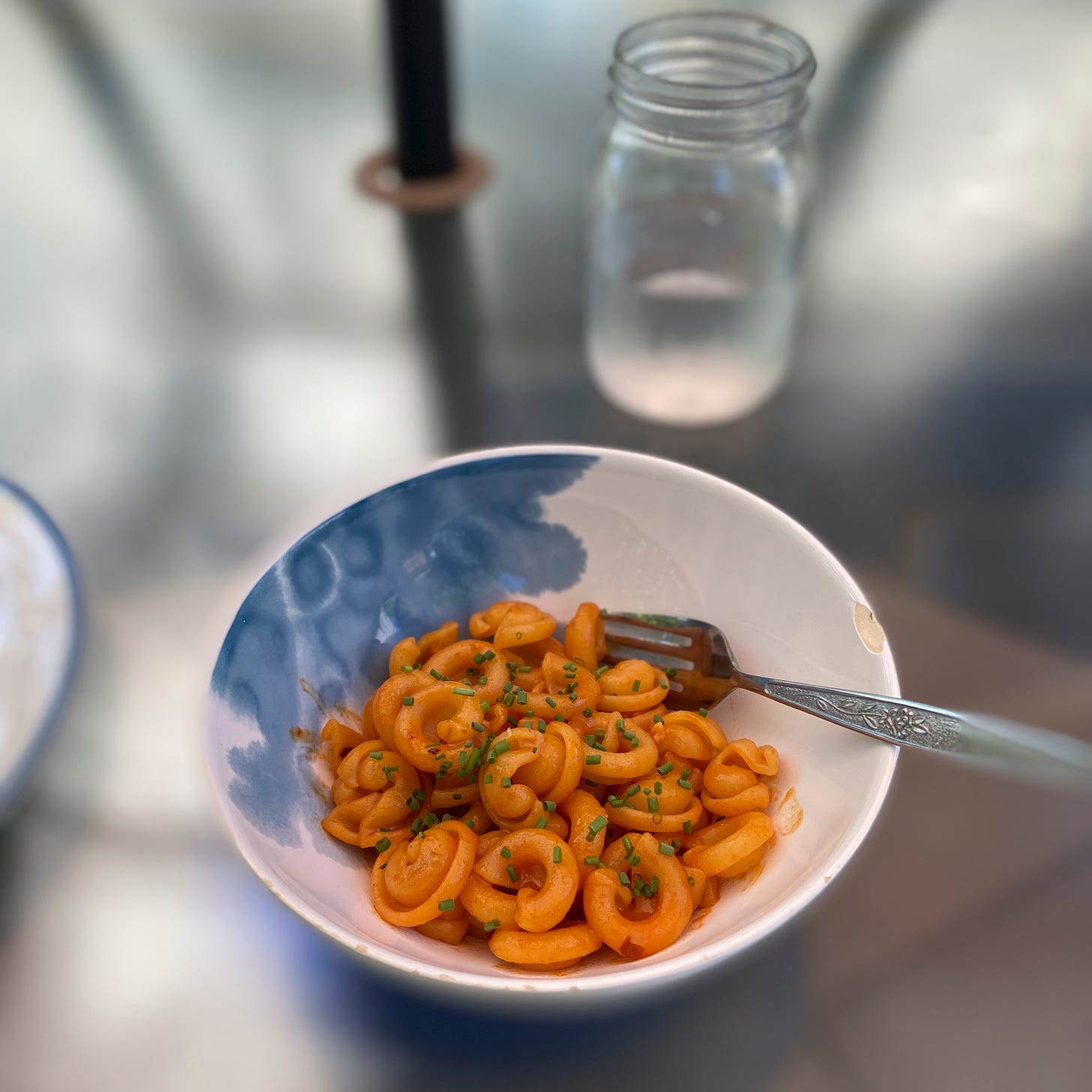 A blue and white bowl of cappelletti in a deep orange sauce, with finely chopped chives on top. A glass of water sits on the table above and to the right.
