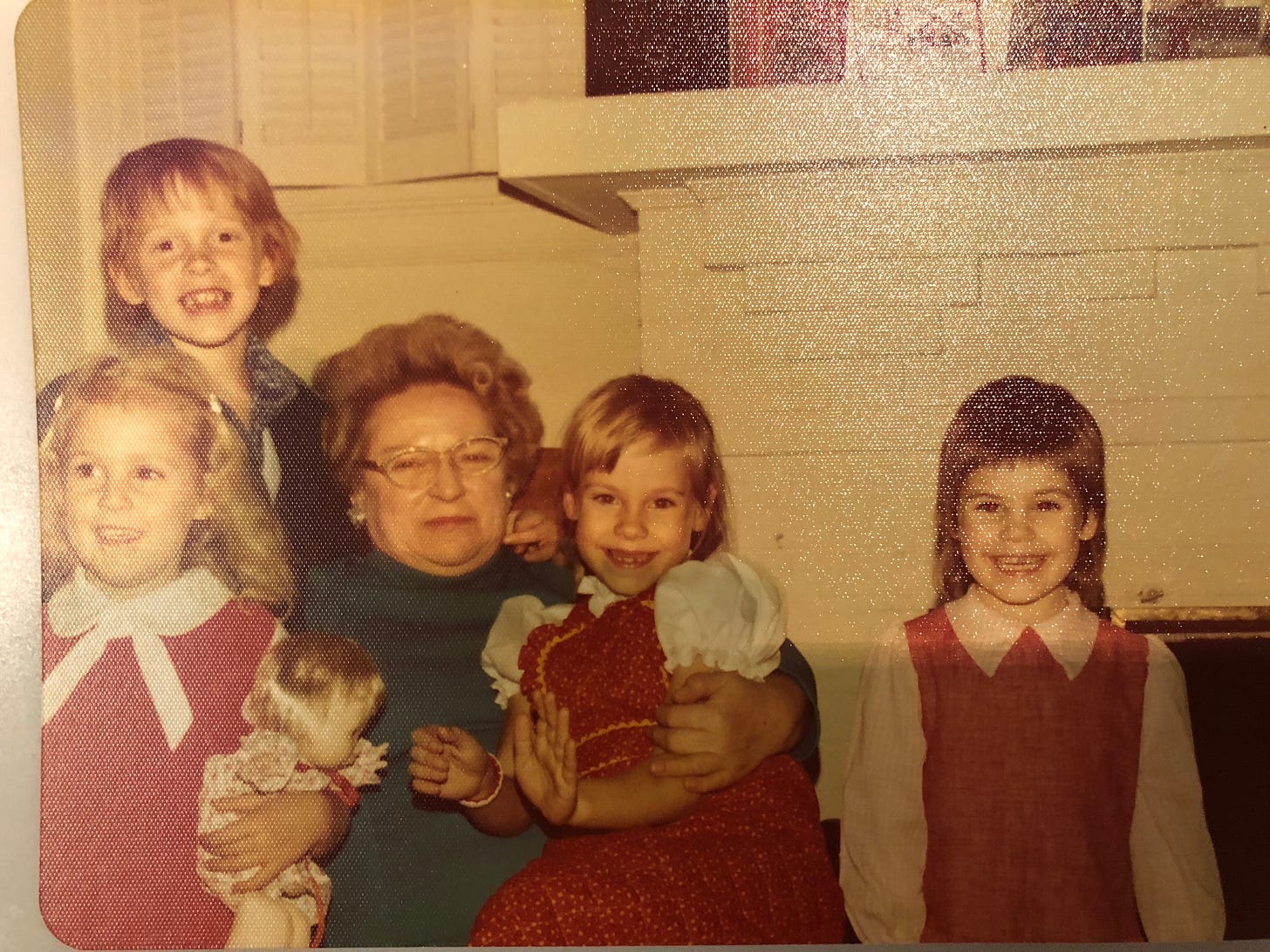 Family gathering in front of a white brick fireplace with a grandmother wearing glasses and four grandchildren (one boy, 3 girls) ages 4-8. 