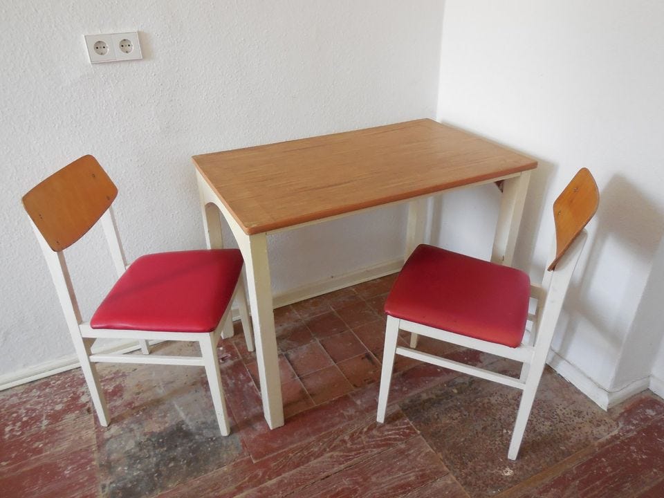 Two white chairs with red seats and a matching table with white legs and a wooden surface.