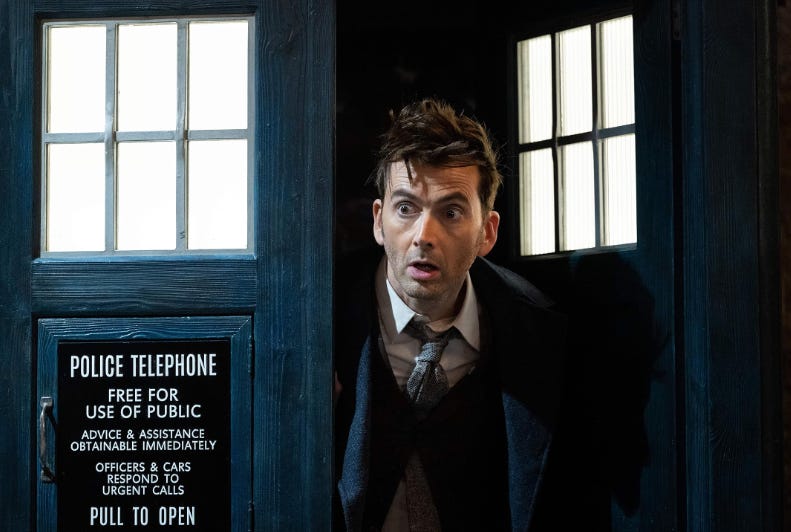 O ator David Tennant sai da Tardis, o veículo de Doctor Who em formato de cabine de polícia; ele te uma expressão de surpresa no olhar.