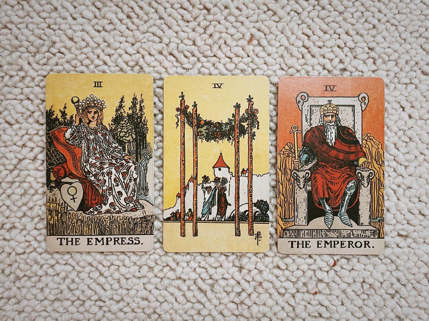 Image depicts three tarot cards, from left: The Empress, the four of Wands, and the Emperor