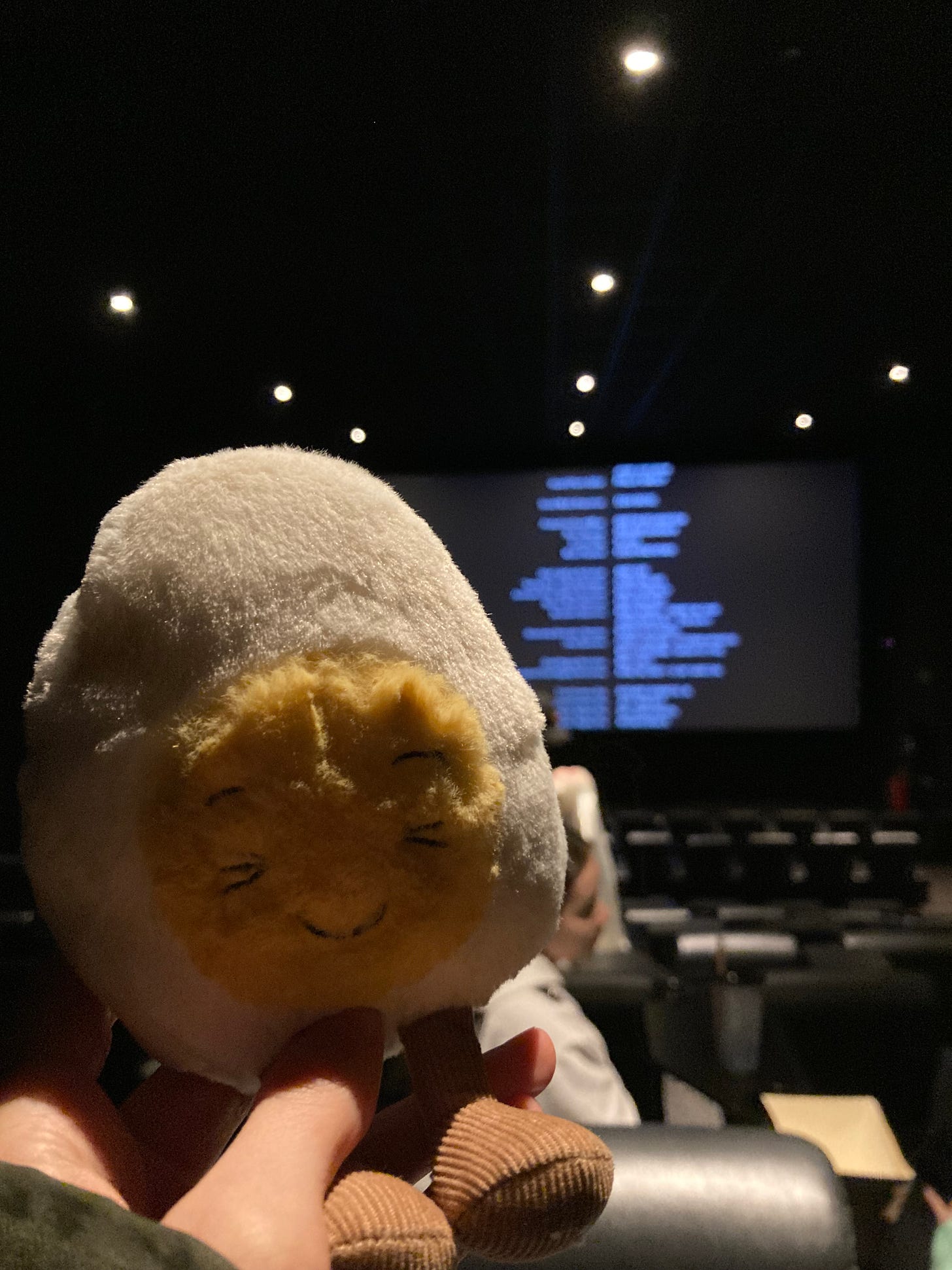 photograph of Dippy the soft toy egg in a dark cinema as credits roll in the background on the big screen