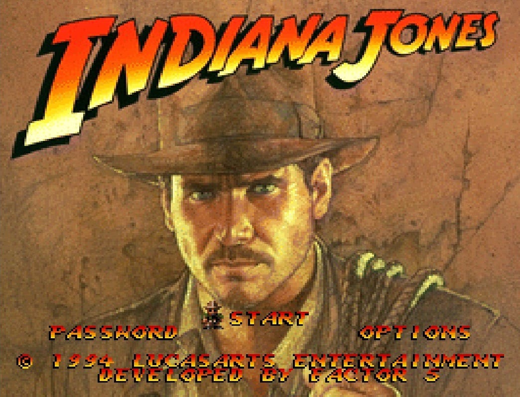 A screenshot of the title screen of Indiana Jones' Greatest Adventures, with the Indiana Jones font/logo above, art of Indy staring out at the screen in the center, and all of it made to look like it's on an old-timey map, in terms of the grime/weathering/coloring of it all. There's a small, chibi Indy sprite used to show whether you're on "Start" or "Password" or "Options"