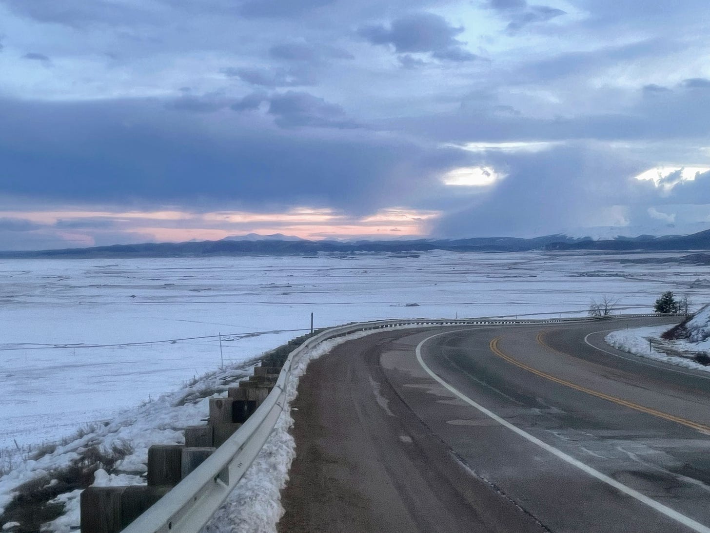 A sunset view of a vast, snowy valley with tall mountain peaks in the distance