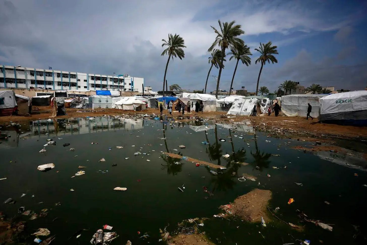 Dozens of white tents and structures surround a giant puddle with trash floating in it.