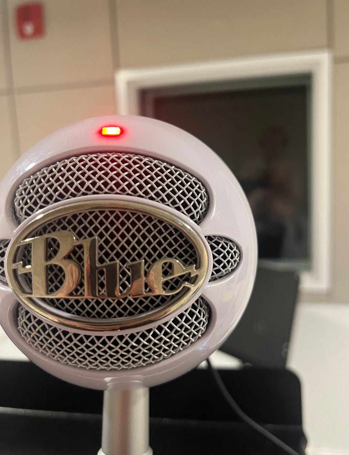 A modern-looking podcasting style microphone that is a round ball with a wire mesh on the front. A red light on the top indicates it's recording