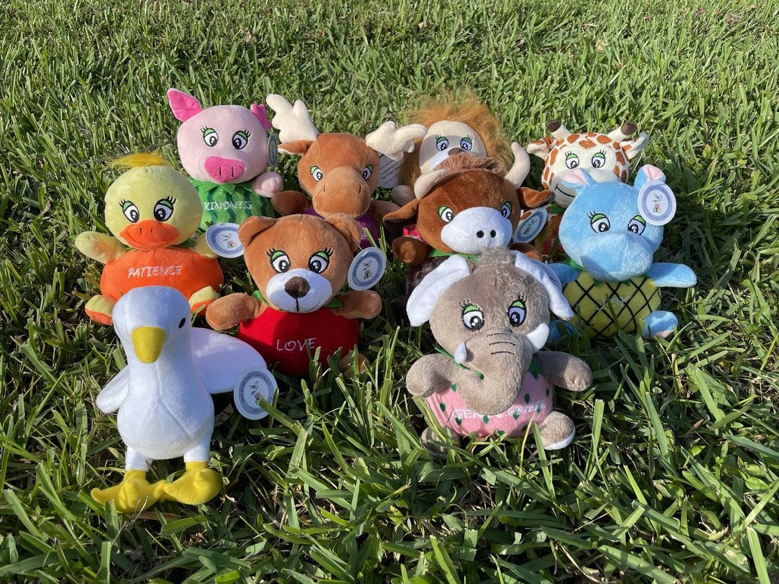 A group of stuffed animals sitting in the grass. They have animals heads and limbs but fruits for bodies and each has a different "fruit of the spirit" written on it. There's also an animal that looks like a goose but is supposed to be a dove.