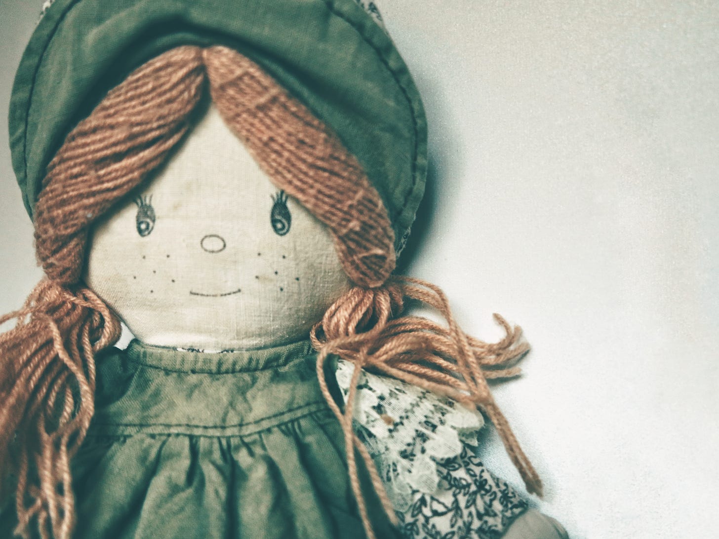 Cloth doll in green hat and dress with brown hair made of yarn.
