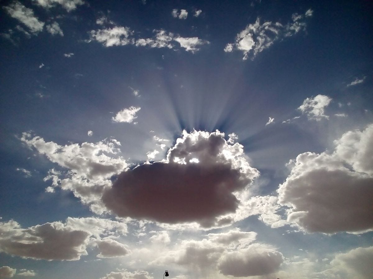 A cloudy sky scape with the sun behind a cloud and light rays shining out from the cloud