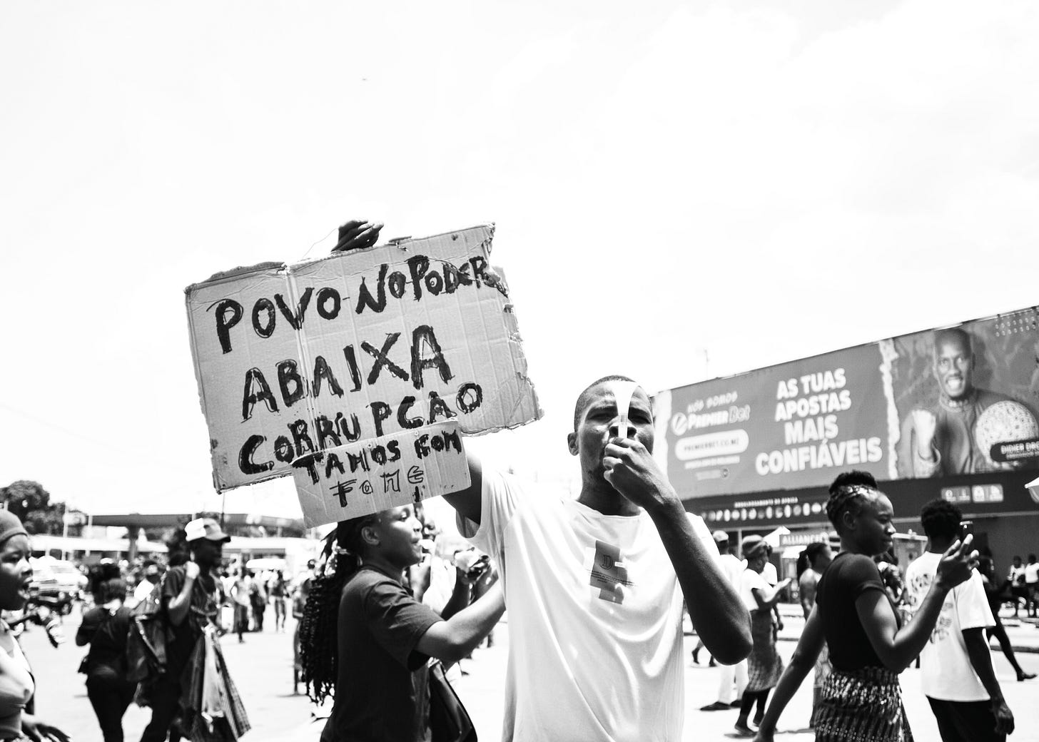 A group of protestors in the street. One of them holding a sign saying people in power, remove corruption, and blowing a whistle