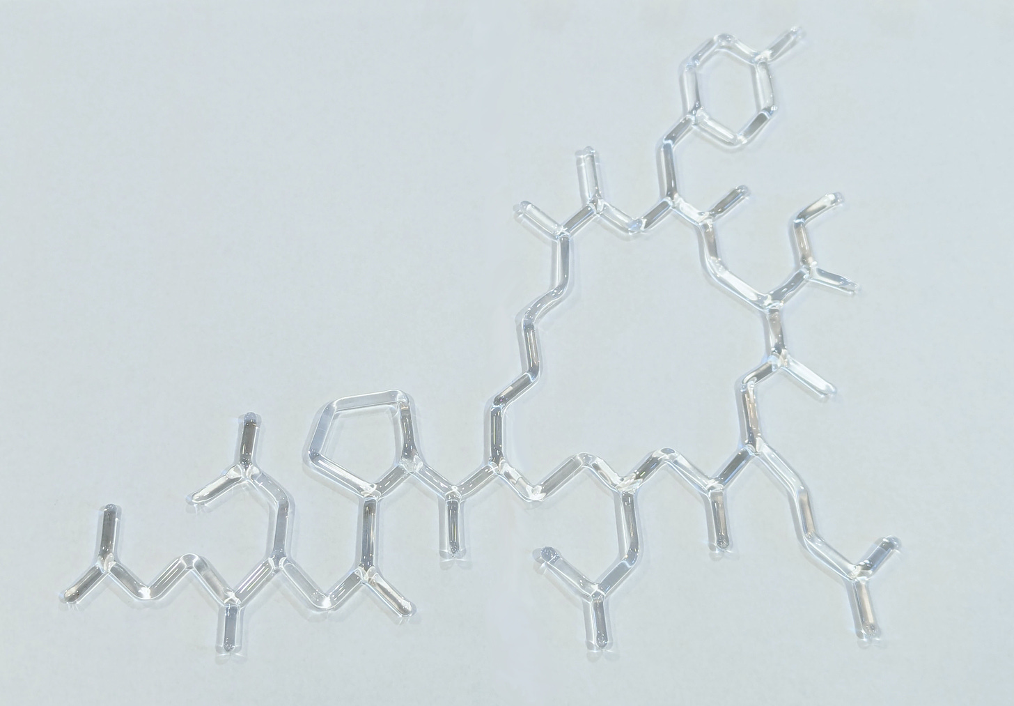 A clear glass molecular model of a complex organic compound on a white background. The model shows various atoms connected by bonds, forming rings and branches typical of large organic molecules.