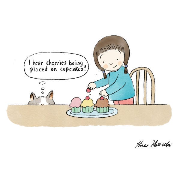 The frame shows a girl with brown hair wearing a blue sweater who is standing on a chair placing cherries on cupcakes. "I hear cherries being placed on cupcakes!" thinks the grey and white cat peeking at the cupcakes from under the table.