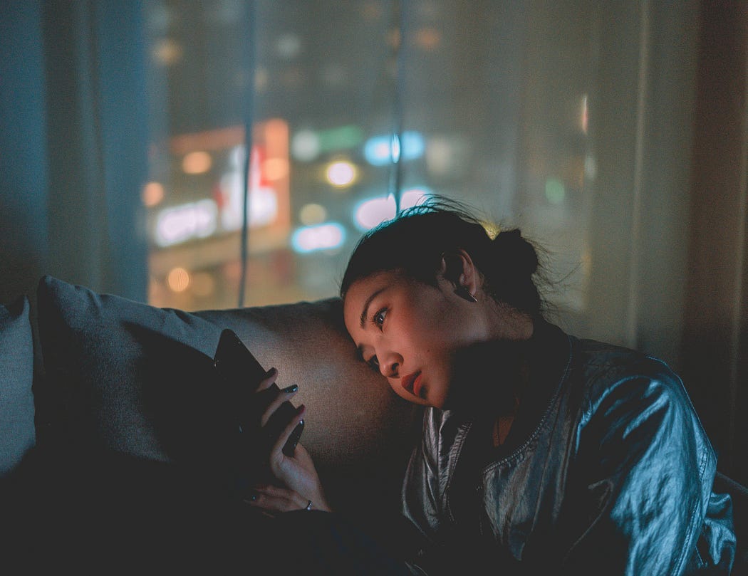 Young woman looking at her phone in the dark with city lights in the background